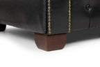Close-up of black leather Chesterfield sofa corner with gold nailhead trim and wooden leg