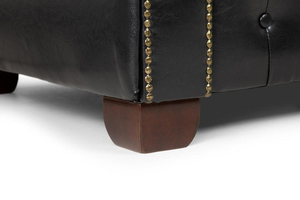 Close-up of black leather sofa with gold stud accents and wooden legs