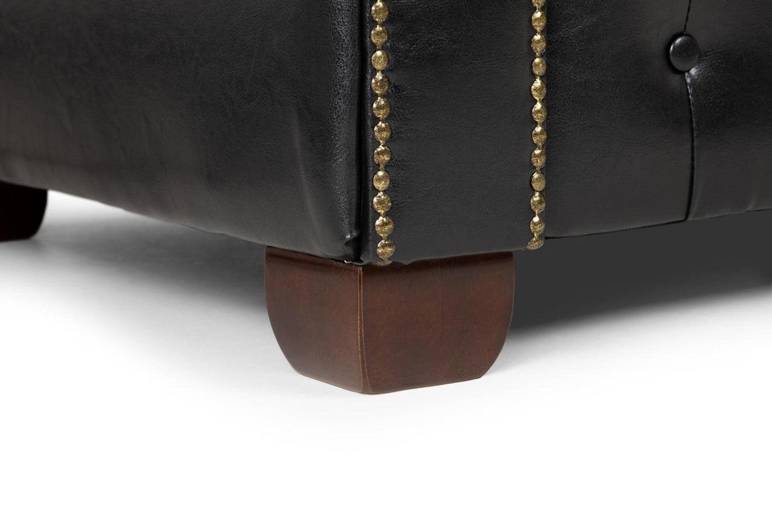 Close-up of black leather sofa with gold stud accents and wooden legs