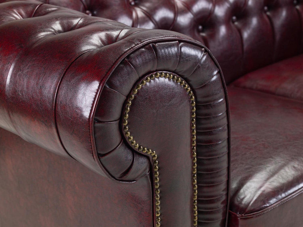 Close-up of oxblood chesterfield leather sofa armrest with button tufting and brass studs