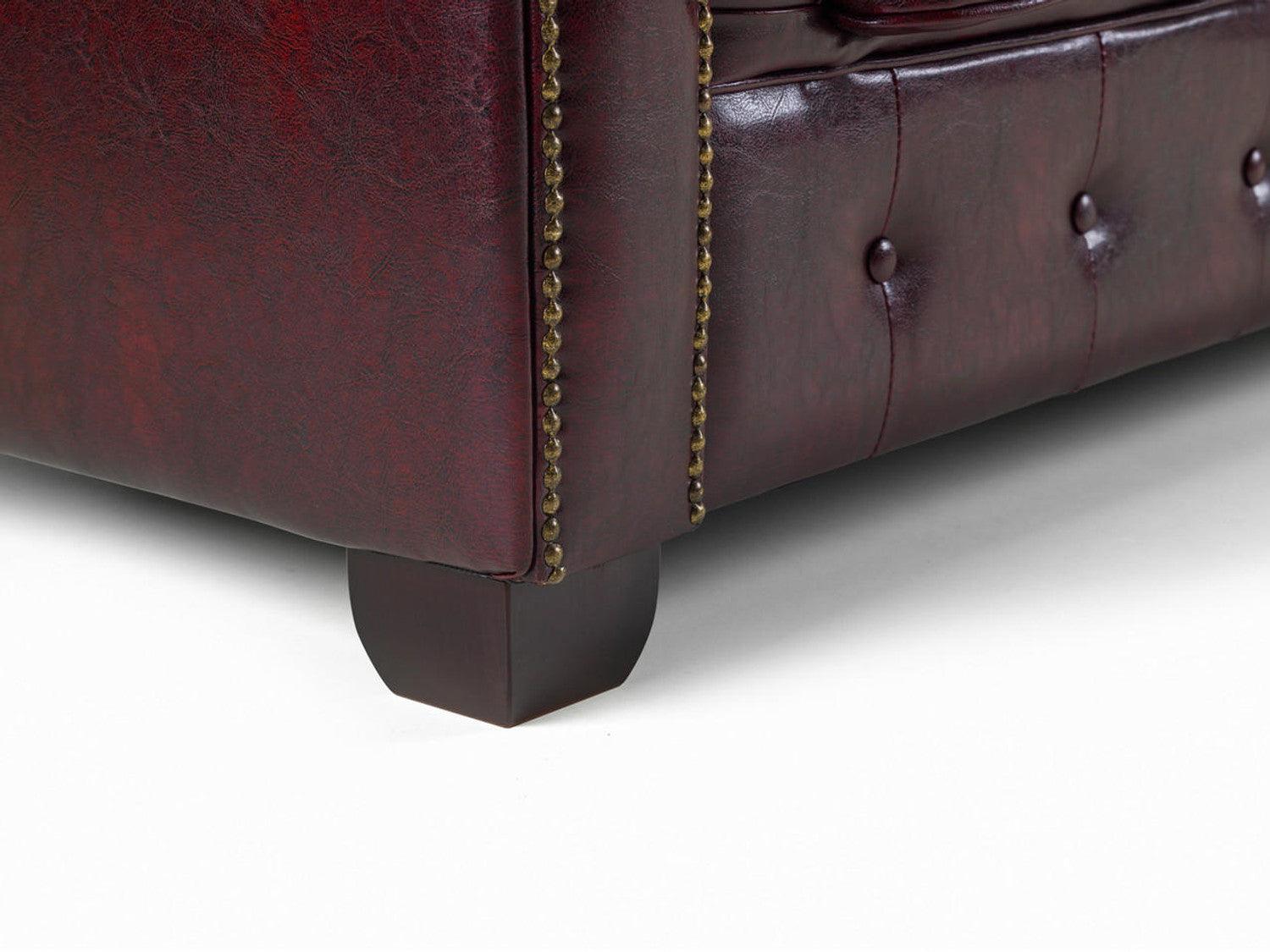 Close-up of oxblood leather Chesterfield sofa with tufted design and brass nailhead trim