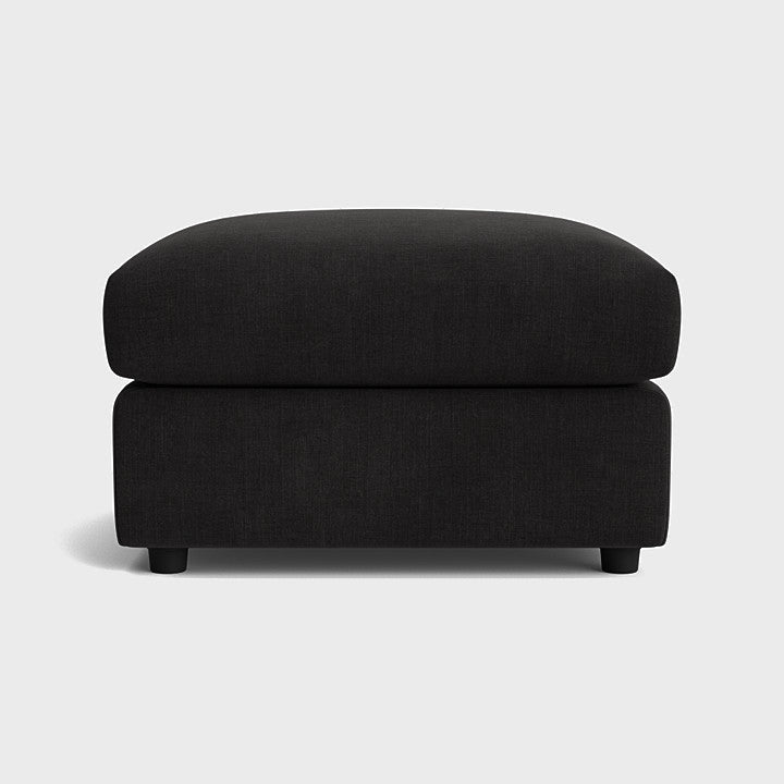Modern black fabric ottoman with soft cushioning on a plain background