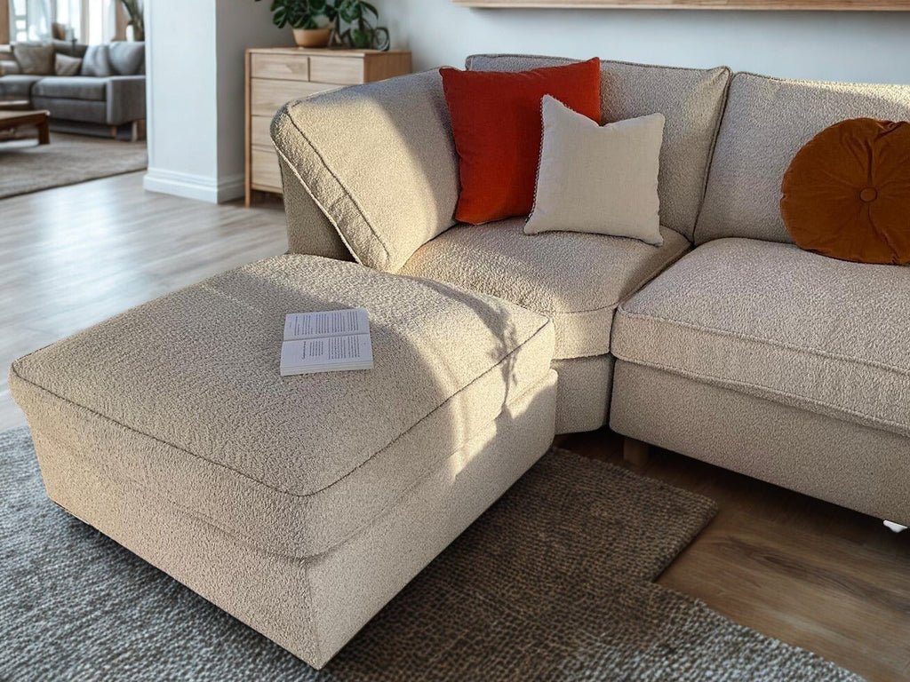 Cream boucle U-shaped sofa with ottoman, colorful cushions, and an open book in a modern living room