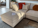 Cream boucle U-shaped sofa with ottoman, colorful cushions, and an open book in a modern living room