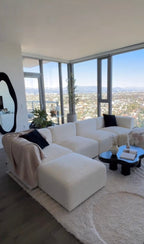 Cream boucle modular U-shape sofa with footstools in a modern living room with city view