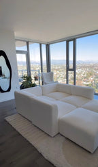 Cream boucle modular U-shape sofa with footstools in a modern living room with city view