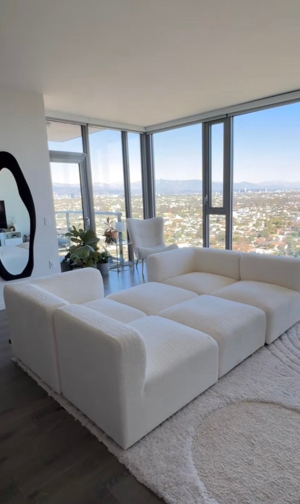 Cream boucle modular U-shaped sofa in modern living room with large windows and city view
