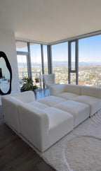 Cream boucle modular U-shaped sofa in modern living room with large windows and city view