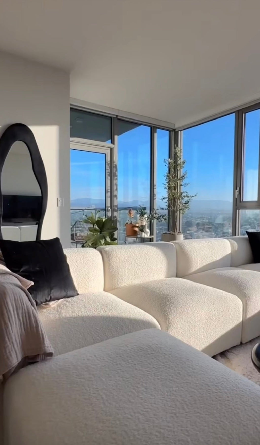 Modern living room with cream boucle modular U-shape sofa, large windows, and plants