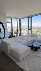 Cream boucle modular U-shaped sofa with footstools in modern living room, city view windows