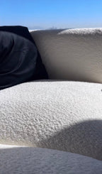 Cream boucle sofa with textured upholstery in natural sunlight, partial black cushion visible