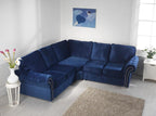 Blue velvet corner sofa with full back cushions in a bright living room, next to a window.