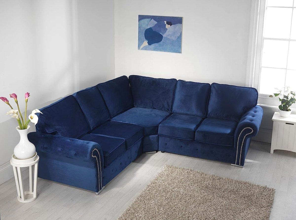 Blue velvet corner sofa with full back cushions in a bright living room, next to a window.
