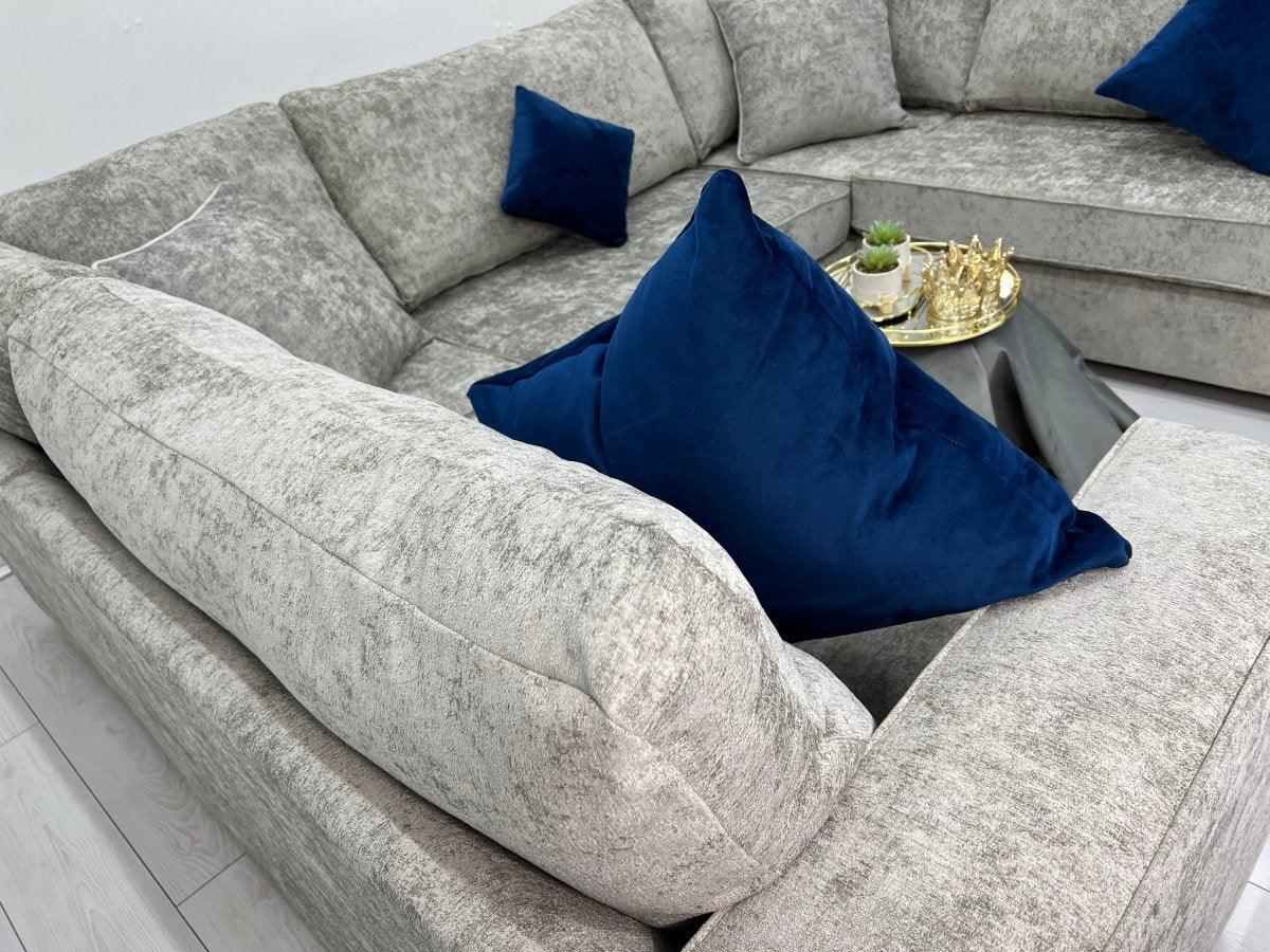 Modern U-shaped grey sofa with blue velvet cushions and a gold tray on a black table