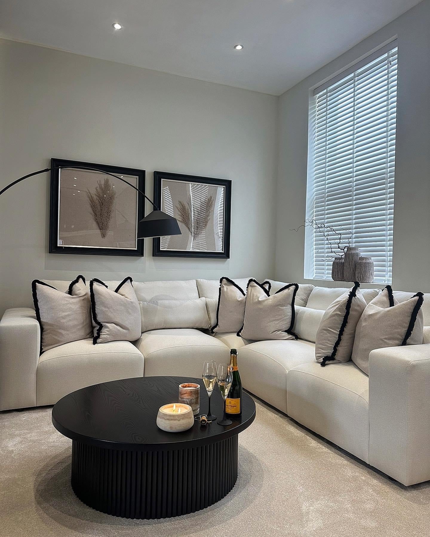 Modern living room with a large cream corner sofa, black coffee table, and neutral decor.