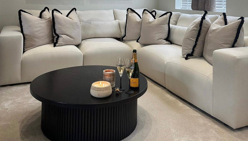 Modern cream corner sofa with black-trim pillows and round black coffee table in living room