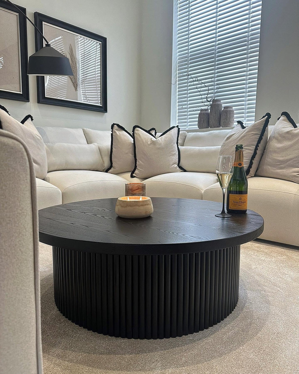 Modern living room with large cream corner sofa, black round coffee table, and decorative cushions.