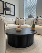 Modern living room with large cream corner sofa, black round coffee table, and decorative cushions.