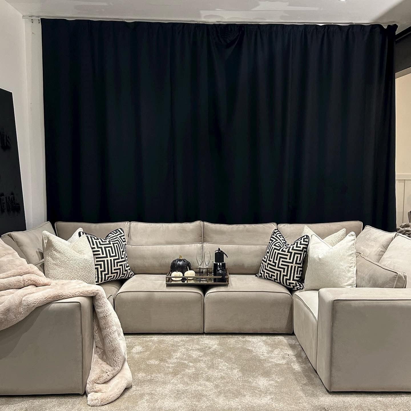 Large cream U-shaped sofa with geometric cushions, throw blanket, and tray in a modern living room.