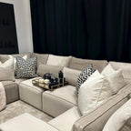 Modern U-shaped cream sofa with plush and geometric pillows, decorative tray on seat.