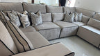 Large U-shaped cream sofa with black piping and patterned scatter cushions in a modern living room