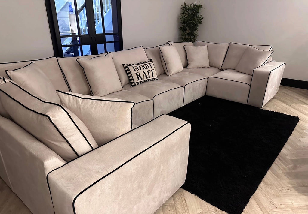 Large cream U-shaped sofa with black piping in a modern living room, black rug, and throw pillows