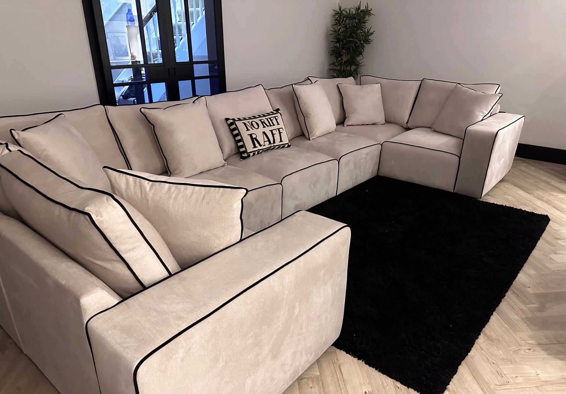 Large cream U-shaped sofa with black piping in a modern living room, black rug, and throw pillows