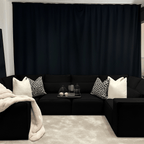 Large U-shaped black sectional sofa with cream and patterned cushions, throw blanket, and tray decor in a modern living room.