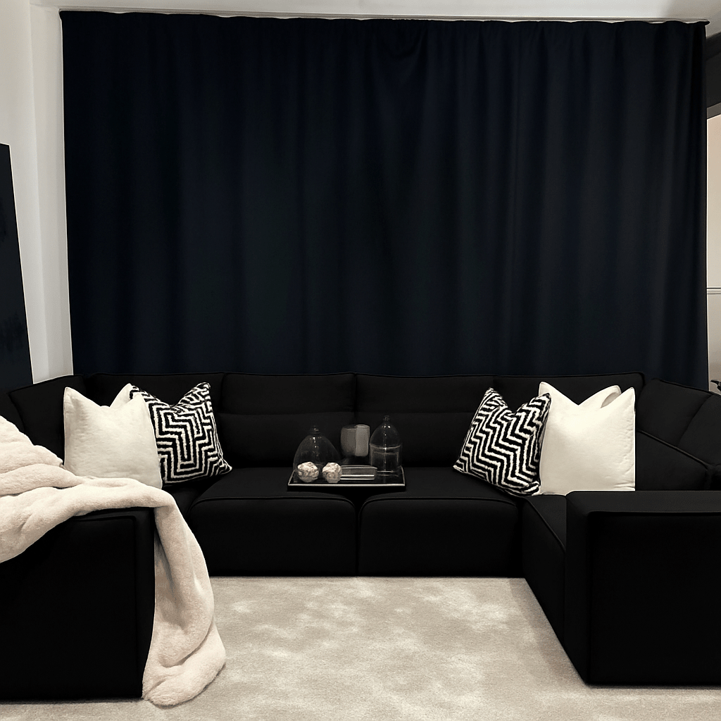 Large U-shaped black sectional sofa with cream and patterned cushions, throw blanket, and tray decor in a modern living room.