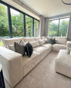 Latte modular corner sofa with black and striped cushions in modern living room with large windows.