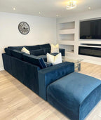Modern living room with large navy modular corner sofa, cream pillows, wall clock, and mounted TV.