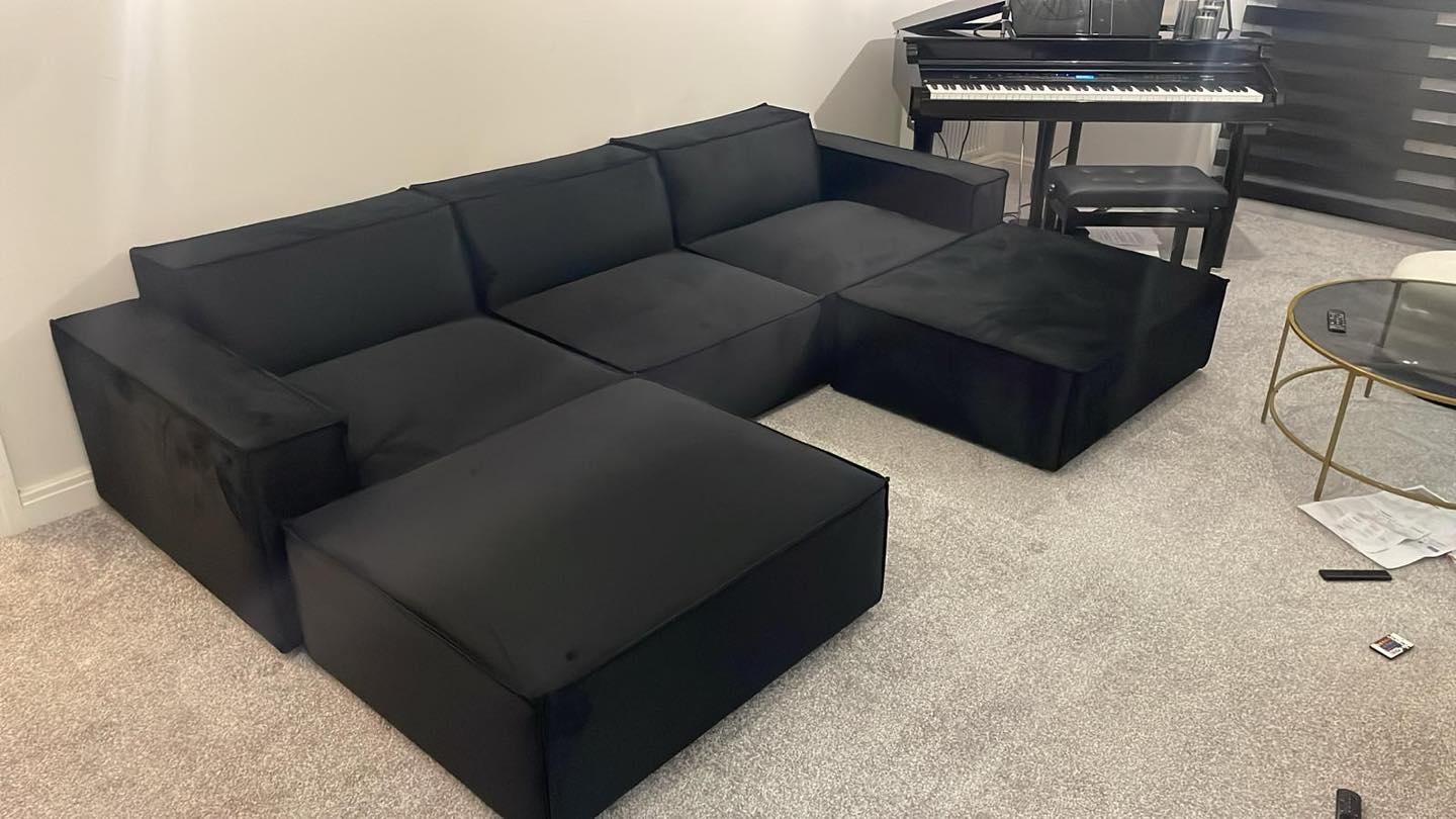 Large black sectional sofa with removable footstool in modern living room with piano