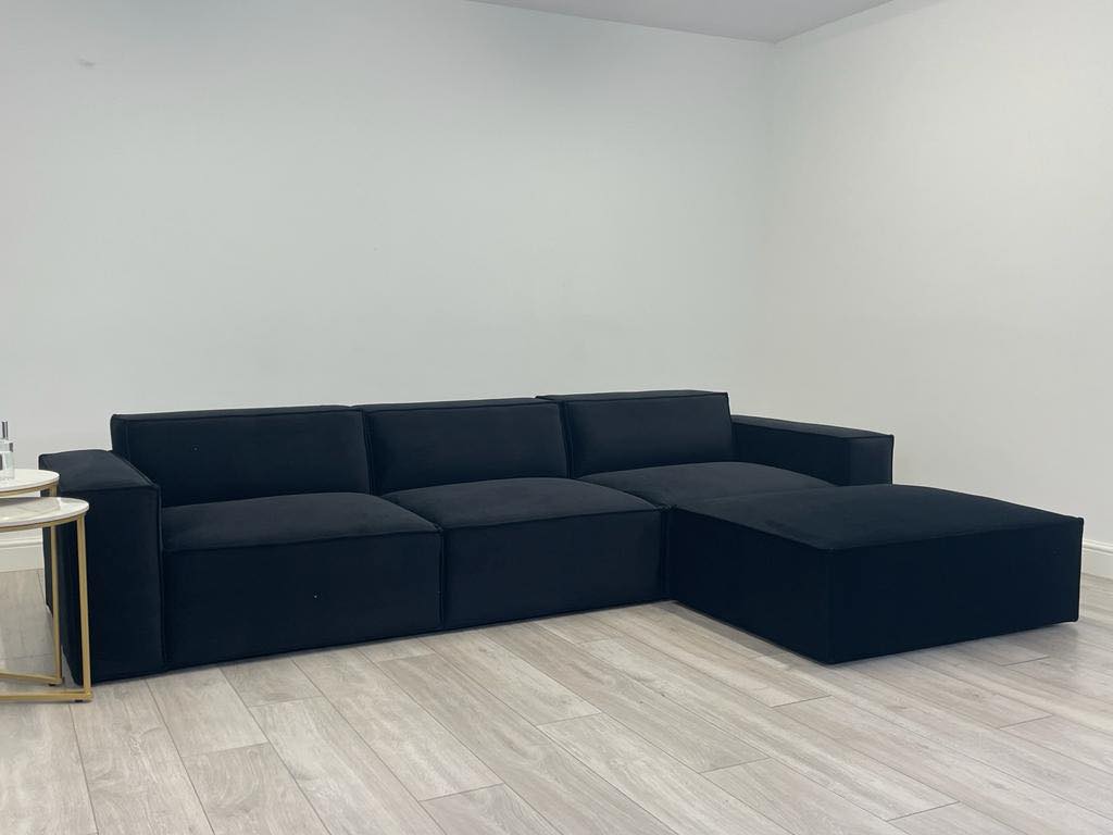 Modern black corner sofa with chaise lounge in a minimal living room on wooden flooring