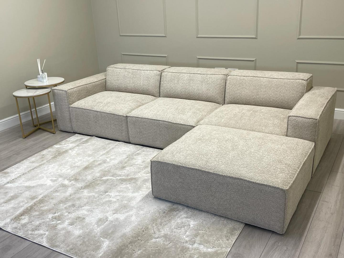 Modern ivory corner sofa with removable footstool on light rug in minimalist living room