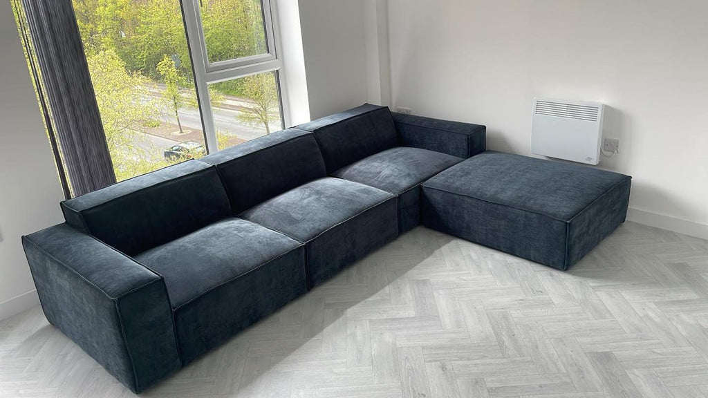 Modern dark blue L-shaped sofa with large removable footstool in a bright living room