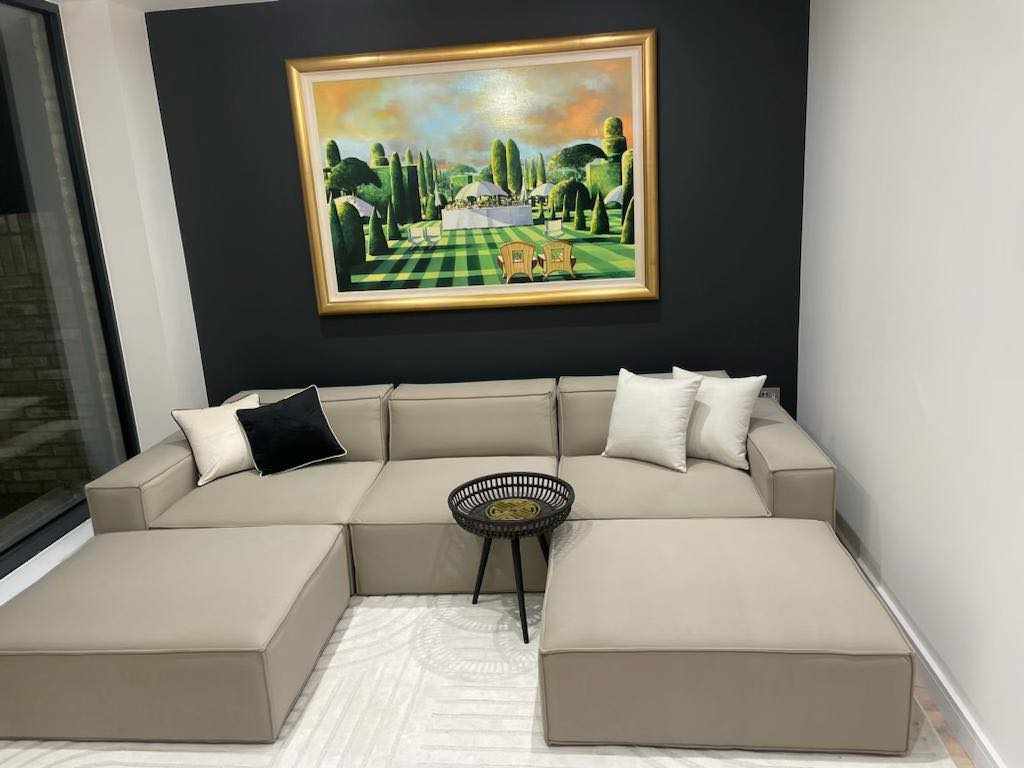 Ivory modular corner sofa with removable footstools, black accent wall, and modern artwork
