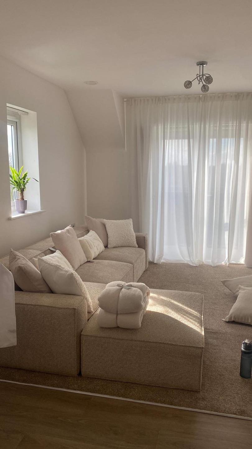 Ivory corner sofa with removable footstool in a bright living room with sheer curtains and neutral decor