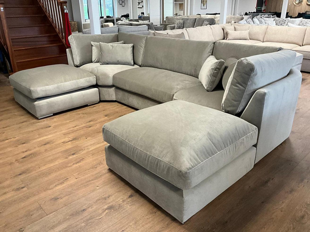 Large U-shaped silver velvet sofa with full back and scatter cushions in a modern showroom
