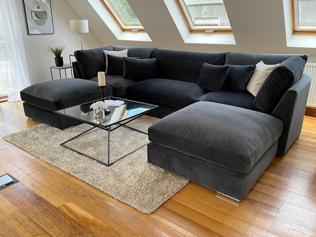 Large U-shaped dark grey velvet sofa with full back, scatter cushions, and glass coffee table in modern living room