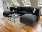 Large U-shaped dark grey velvet sofa with full back, scatter cushions, and glass coffee table in modern living room