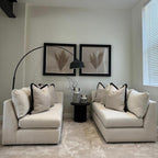 Modern living room with two cream sofas, black trim pillows, round side table, and minimalist decor