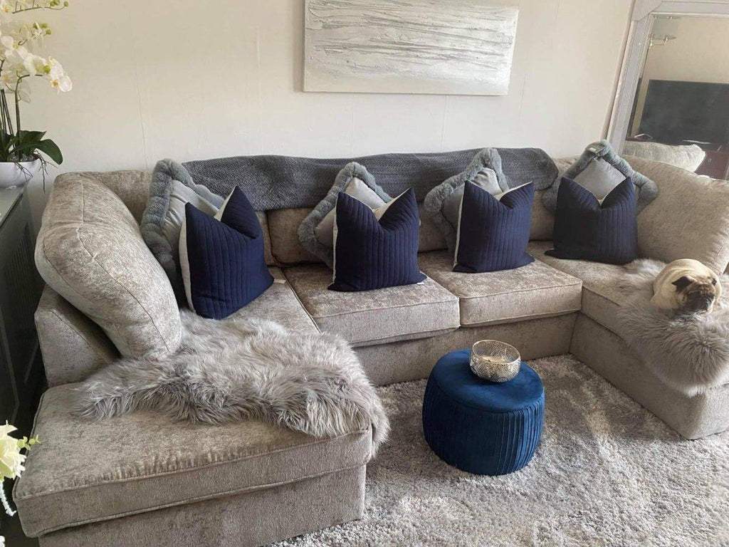 U-shape beige sectional sofa with navy pillows, faux fur throws, and blue ottoman in a modern living room.