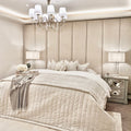Cream velvet upholstered headboard wall panels behind a stylishly dressed bed with soft bedding.