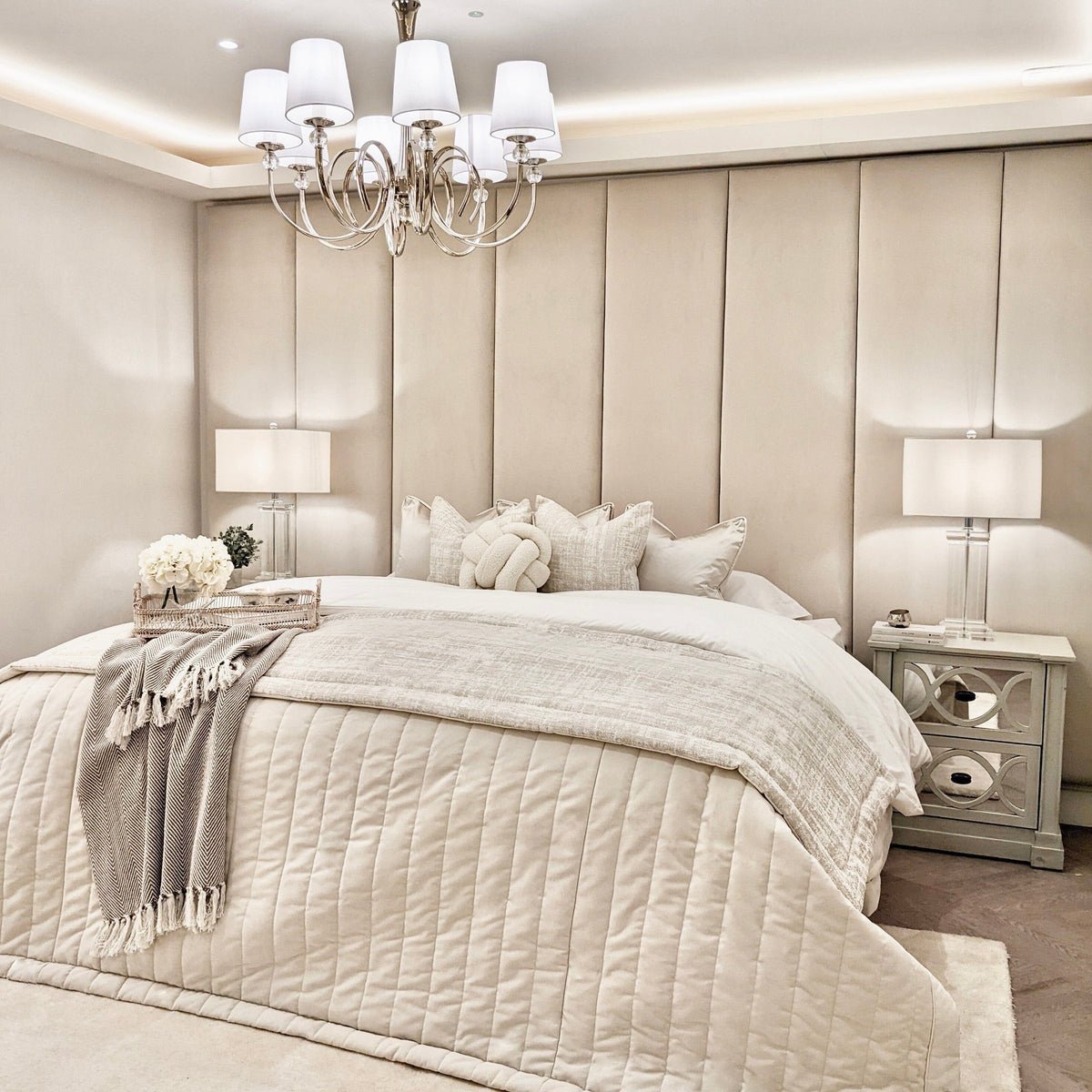 Cream velvet upholstered headboard wall panels behind a stylishly dressed bed with soft bedding.