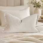 Cream velvet ruffle pillow on luxury bed with textured bedding and floral vase