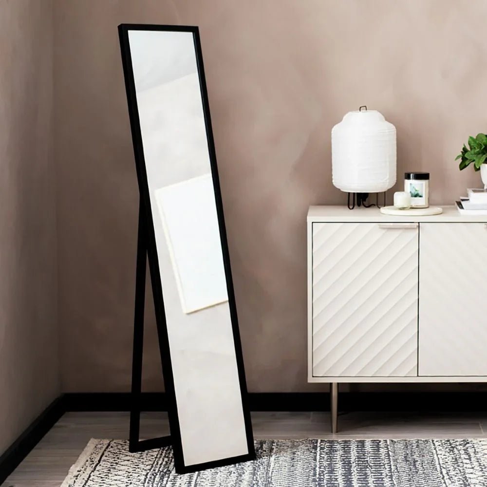 Black full-length floor mirror with A-frame stand in modern living room, beside white sideboard and lamp