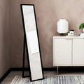 Black full-length floor mirror with A-frame stand in modern living room, beside white sideboard and lamp