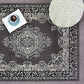 Grey vintage-style area rug with intricate floral pattern, styled with book, coffee cup, and knit pouf for cozy living room decor.
