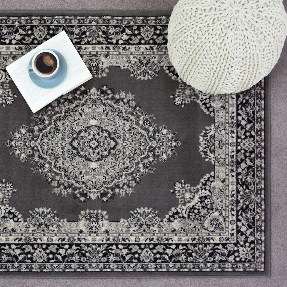 Grey vintage-style area rug with intricate floral pattern, styled with book, coffee cup, and knit pouf for cozy living room decor.