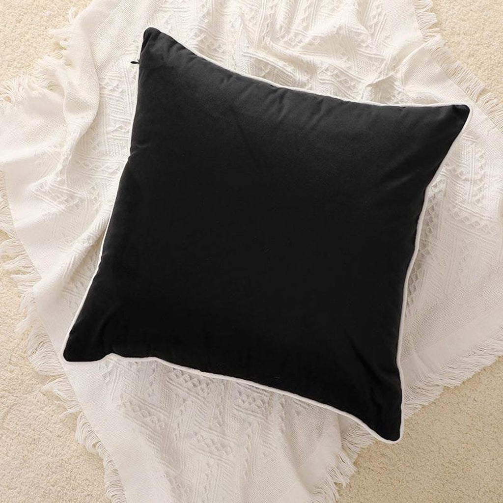 Black velvet cushion with white piping on textured cream throw blanket